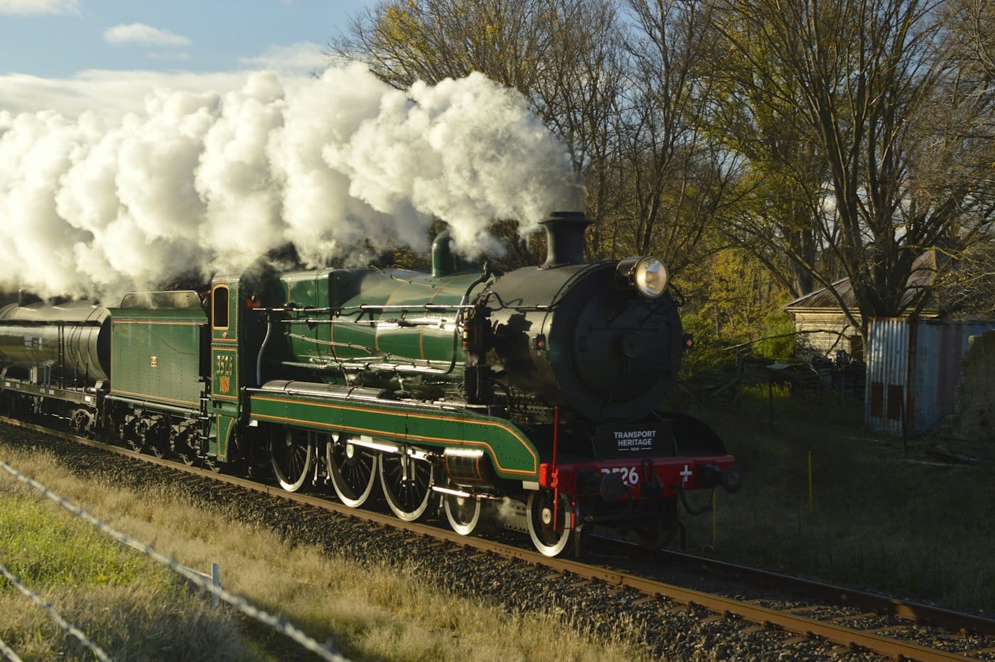 Vintage steam train with white smoke rolling through the countryside